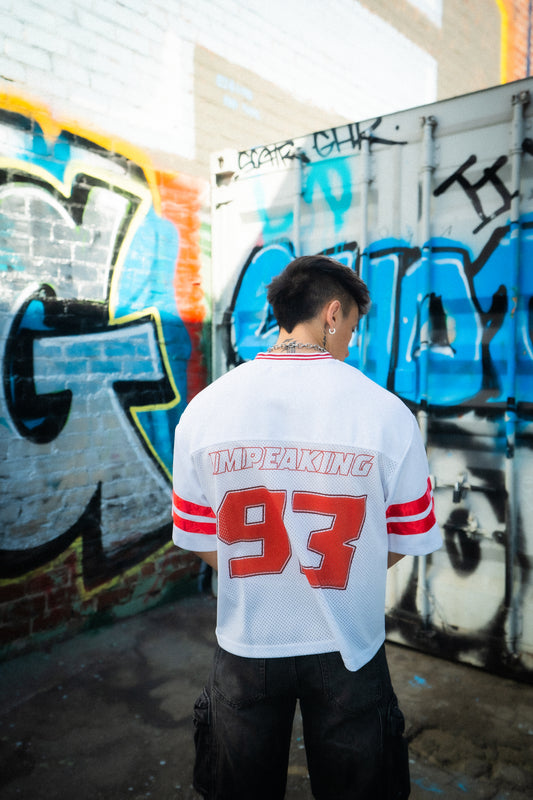 Model wearing white and red PLUR 1993 Raver Manifesto Jersey in front of graffiti wall, rave streetwear festival outfit. IM PEAKING