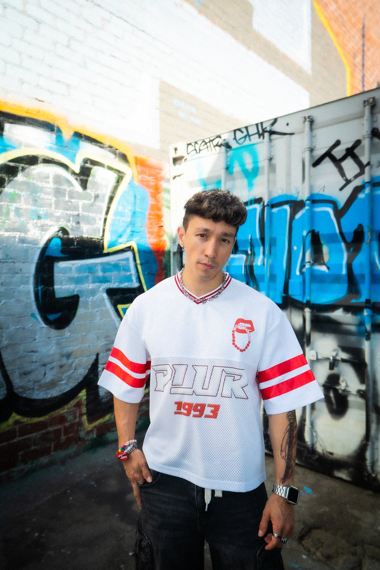 Model wearing white and red PLUR 1993 Raver Manifesto Jersey in front of graffiti wall, rave streetwear festival outfit