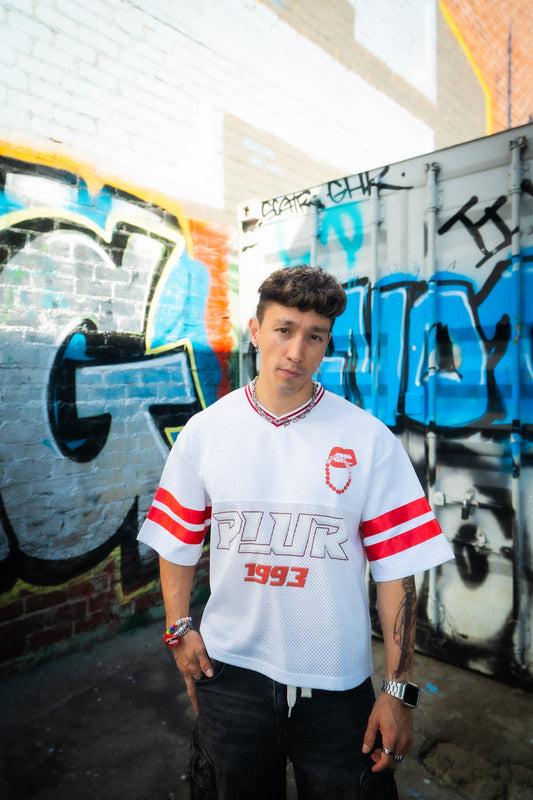 Model wearing white and red PLUR 1993 Raver Manifesto Jersey in front of graffiti wall, rave streetwear festival outfit
